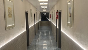 A long, narrow hallway with a polished marble floor, framed artwork on the walls, and recessed lighting on the ceiling. - Hotel Ankur (Diu)