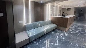 A modern reception area with a marble floor, a reception desk, a bench, and a clock on the wall. - Hotel Ankur (Diu)