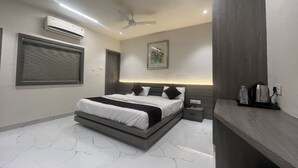 A modern bedroom with a large bed, a ceiling fan, an air conditioning unit, a bedside table with a lamp, and a nightstand. - Hotel Ankur (Diu)
