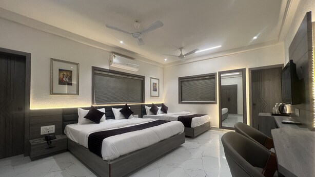 A modern bedroom with a large bed, bedside tables, a ceiling fan, and a TV. - Hotel Ankur (Diu)