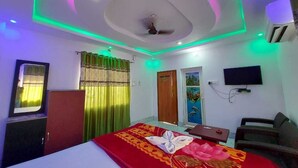 A hotel room with a bed, a desk, a TV, and a ceiling fan. - Swastik Resort (Kanthi)