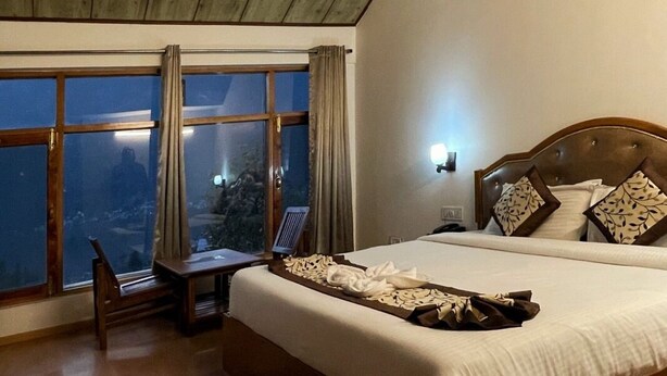 A bedroom with a large bed, a desk, and a window with curtains. - Shreshtam Lakhnpal Resort (Manali)