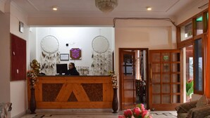 A reception desk with a wooden counter, a computer, and a decorative wall with hanging items. - Shreshtam Lakhnpal Resort (Manali)