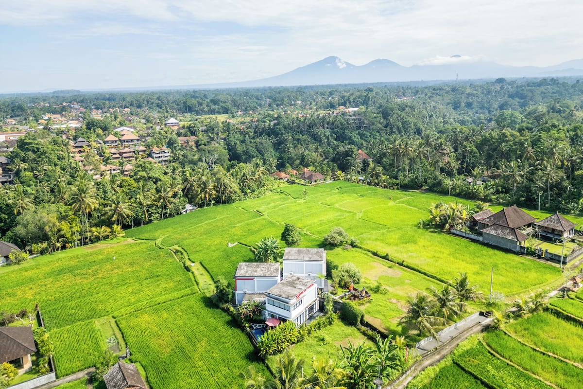A rural landscape with a large green field, a few buildings, and a mountain in the background.
