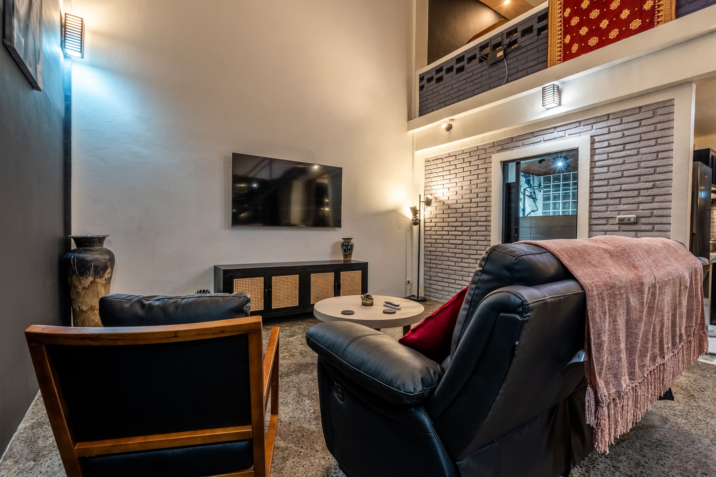 Una sala de estar moderna con un sofá de cuero negro, una silla de madera, una mesa de centro redonda y un jarrón grande.