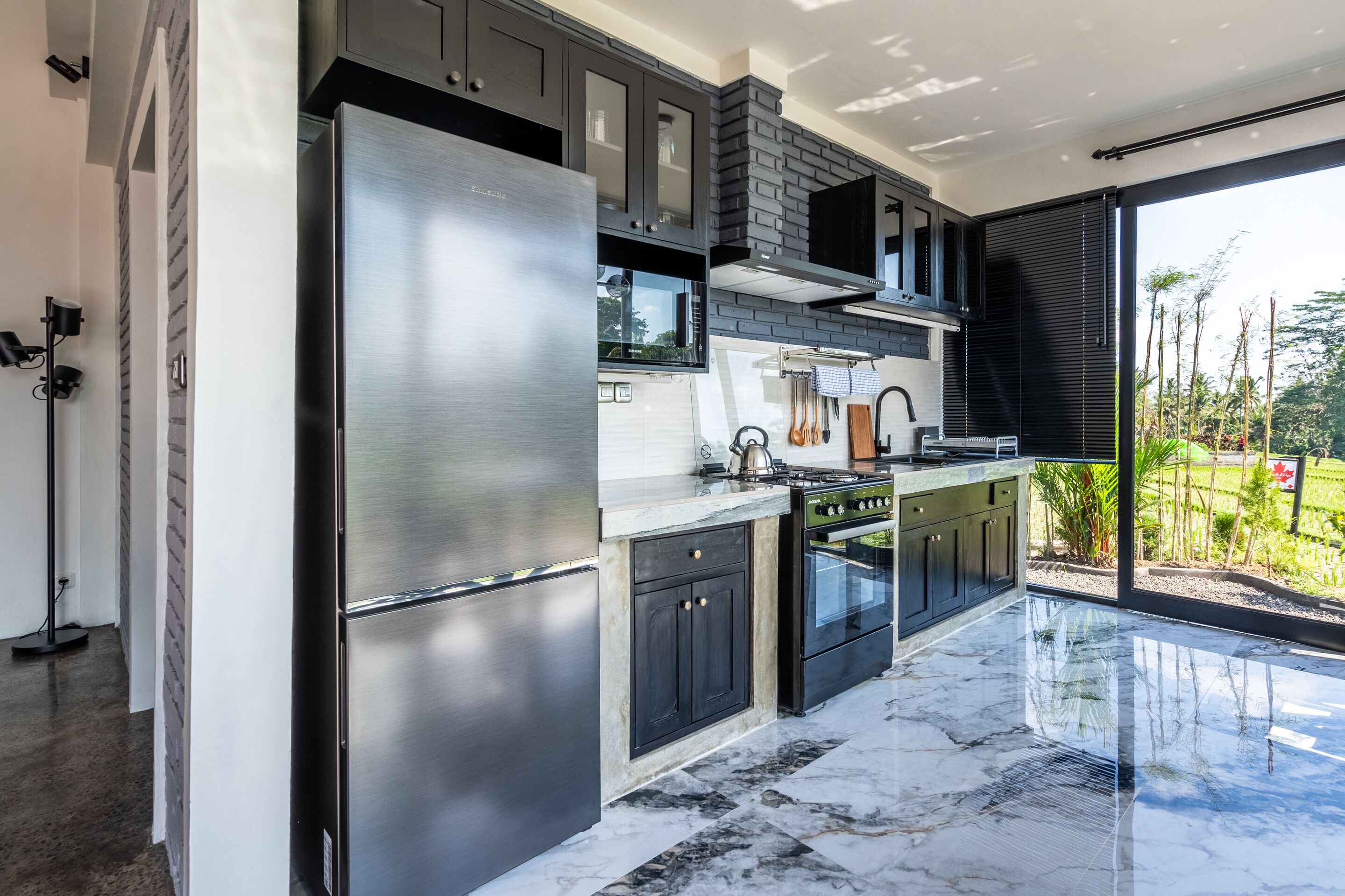 A modern kitchen with stainless steel appliances, dark cabinetry, and a large window offering a view of greenery.