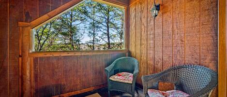 A wooden cabin with a large window overlooking trees, two wicker chairs, and a wooden floor.