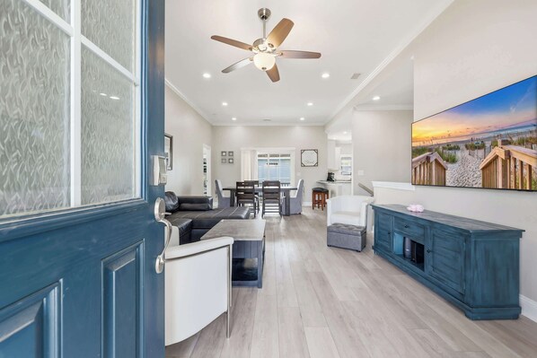 A spacious living area with a ceiling fan, a dining table with chairs, a sofa, and a TV mounted on the wall.