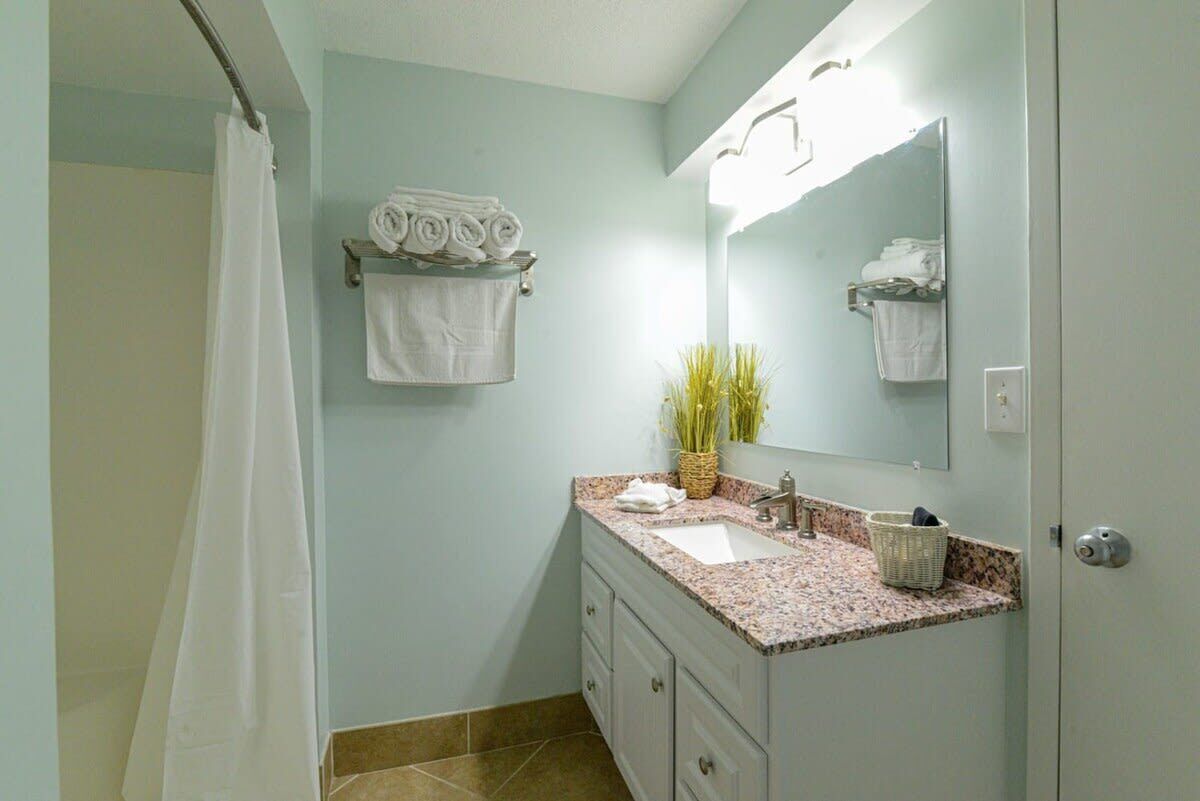 Une salle de bain avec un rideau de douche, un lavabo avec un miroir et des serviettes sur un porte-serviettes.