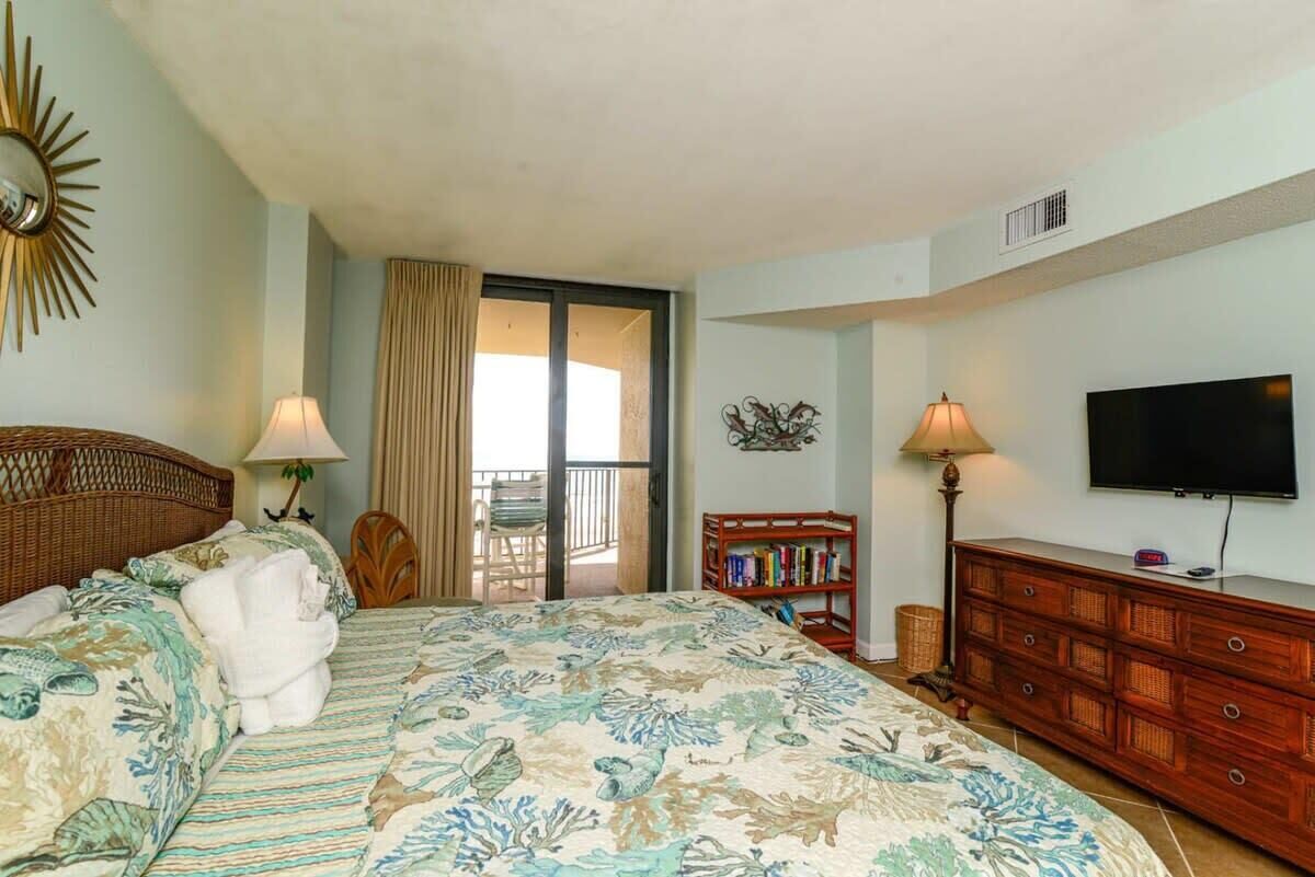 A hotel room with a bed, a television, a bookshelf, and a balcony.