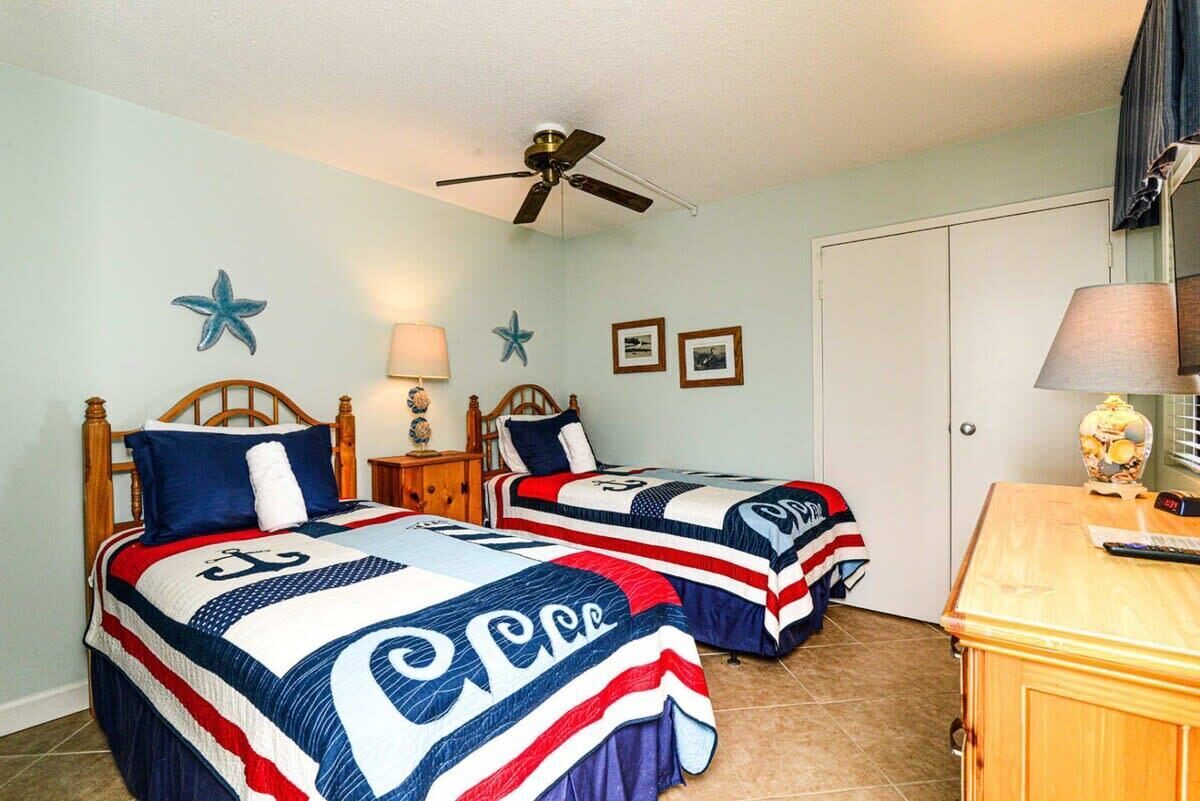 Een slaapkamer met twee bedden, een plafondventilator, decoraties met zeesterren en een houten dressoir.