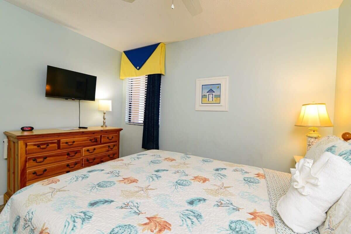 Une chambre à coucher comprenant un lit, une commode, un téléviseur et deux lampes.