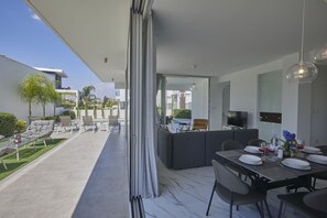 Un área de comedor exterior moderna con un separador de vidrio, una piscina y vistas al vecindario.