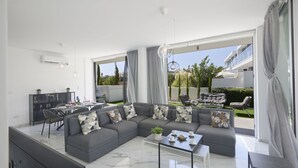 Un salon moderne avec un canapé d’angle, une table basse en verre et un coin repas comprenant une table et des chaises.