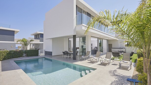 Une maison moderne à deux étages dotée d’une piscine, d’un espace salon extérieur et d’un patio.