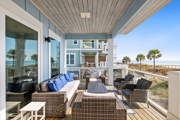A covered outdoor seating area with wicker furniture, a view of the ocean, and a multi-level building in the background. - Blue Heaven on the Beach, Gulf-Front Luxury for Large Groups, Private Pool (Panama City Beach)