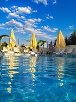 Una piscina con agua azul cristalina, rodeada de sillas de descanso y sombrillas amarillas.