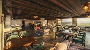 A spacious lounge with wooden tables and green upholstered chairs, a large sofa, and a view of the outdoors. - incebey Konak Cappadocia (Nevsehir)