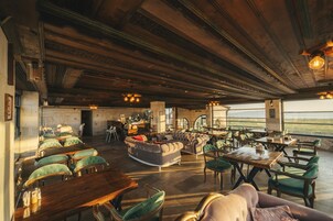 Un salón amplio con mesas de madera y sillones tapizados en verde, un sofá grande y vistas al exterior.
