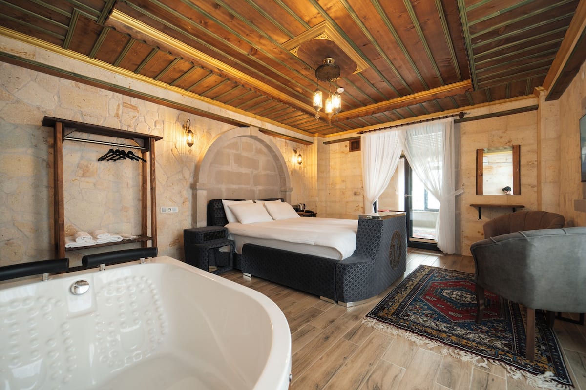 A bedroom with a large bathtub, a bed with a headboard, a desk, and a chair.