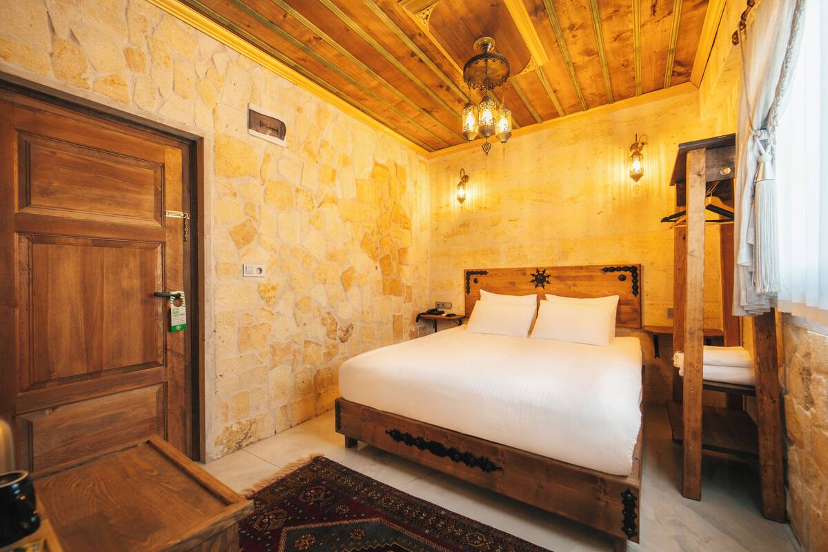 A wooden-framed bed in a stone-walled room with a wooden ceiling and a chandelier.