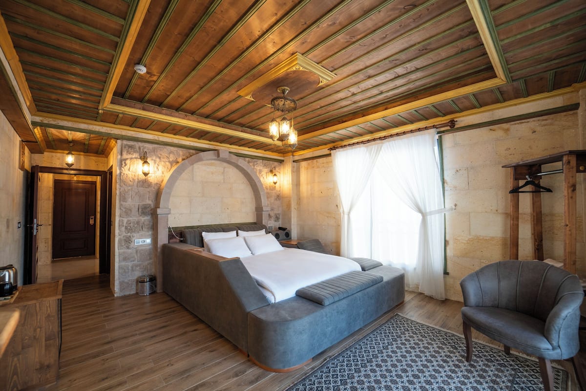 A bedroom with a large bed, a wooden ceiling, stone walls, and a small chair.