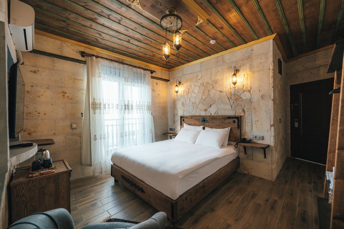 A wooden-framed bedroom with a large bed, stone wall, and a stone fireplace.