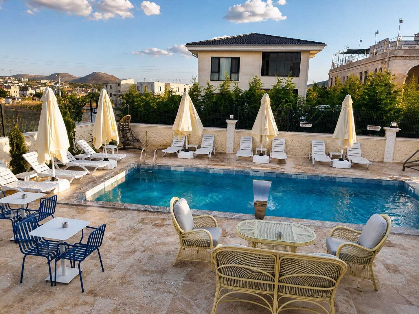 Un área de piscina con sillones de descanso y sombrillas, una mesa con sillas y un edificio al fondo.