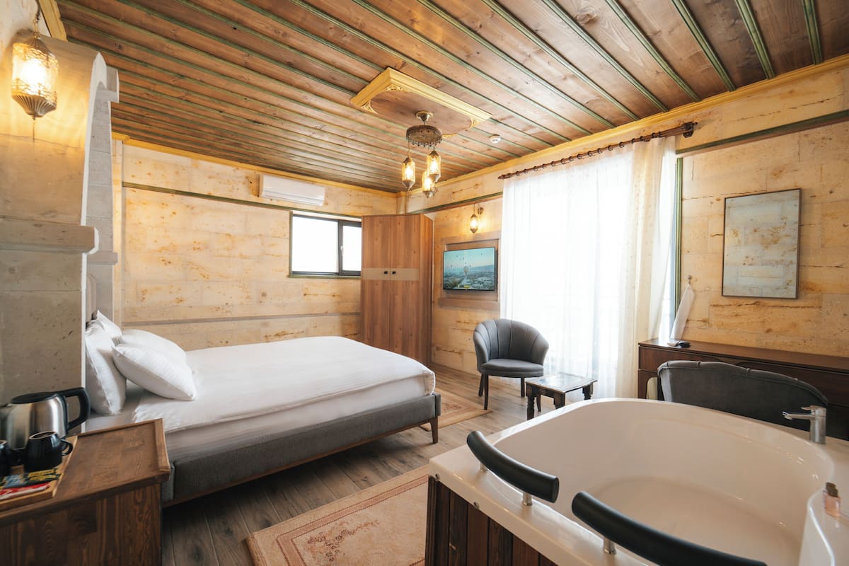 A wooden cabin room with a bed, a chair, a table, a bathtub, and a painting on the wall.