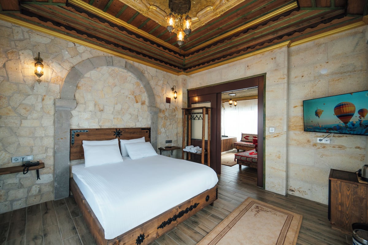A bedroom with a stone wall, wooden bed frame, and a television on the wall.