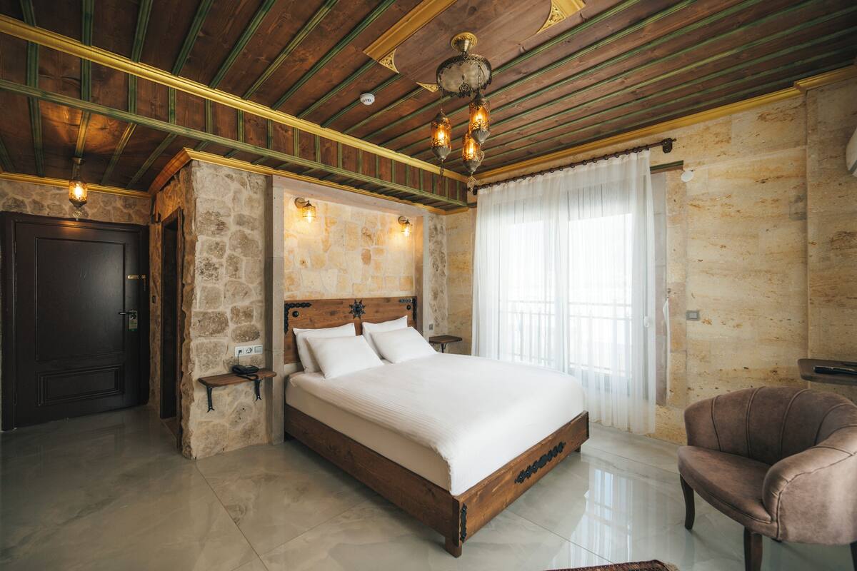 A bedroom with a wooden bed, stone walls, a chandelier, and a leather armchair.