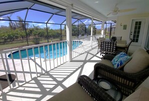 A covered outdoor area with a pool, wicker furniture, and a ceiling fan.
