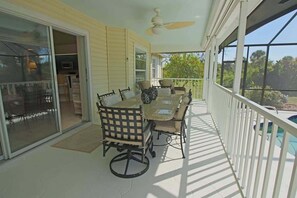 A covered patio with a table and chairs, a ceiling fan, and a view of a swimming pool.