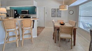 A modern kitchen with teal cabinets, a dining area with wicker chairs, and a large window with blinds. - Sunshine Retreat: SW facing pool, 2 En-Suites #36 (Rotonda West)