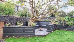 Ein Garten mit einer Holzterrasse, einem Baum und einer Ziegelmauer.
