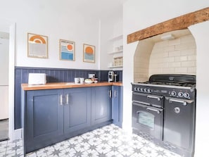 A kitchen with dark blue cabinets, a wooden countertop, a stove, and a tiled backsplash.