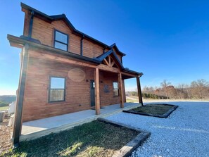 A modern wooden house with a covered porch, a gravel driveway, and a view of the surrounding landscape. - Sunset Ridge- Natural Bridge, Sunset View, Hot Tub (Rogers)