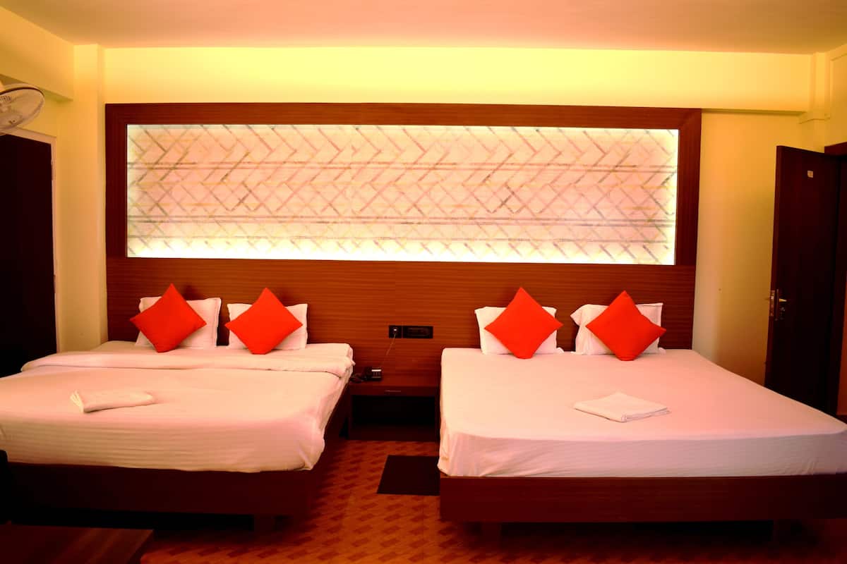 A hotel room with two beds, each with white bedding and red pillows, a large window with a geometric pattern, and a wooden headboard.
