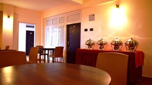 Un comedor con una mesa redonda, sillas y un mantel rojo. Se observan luminarias fijadas a la pared y una puerta al fondo.