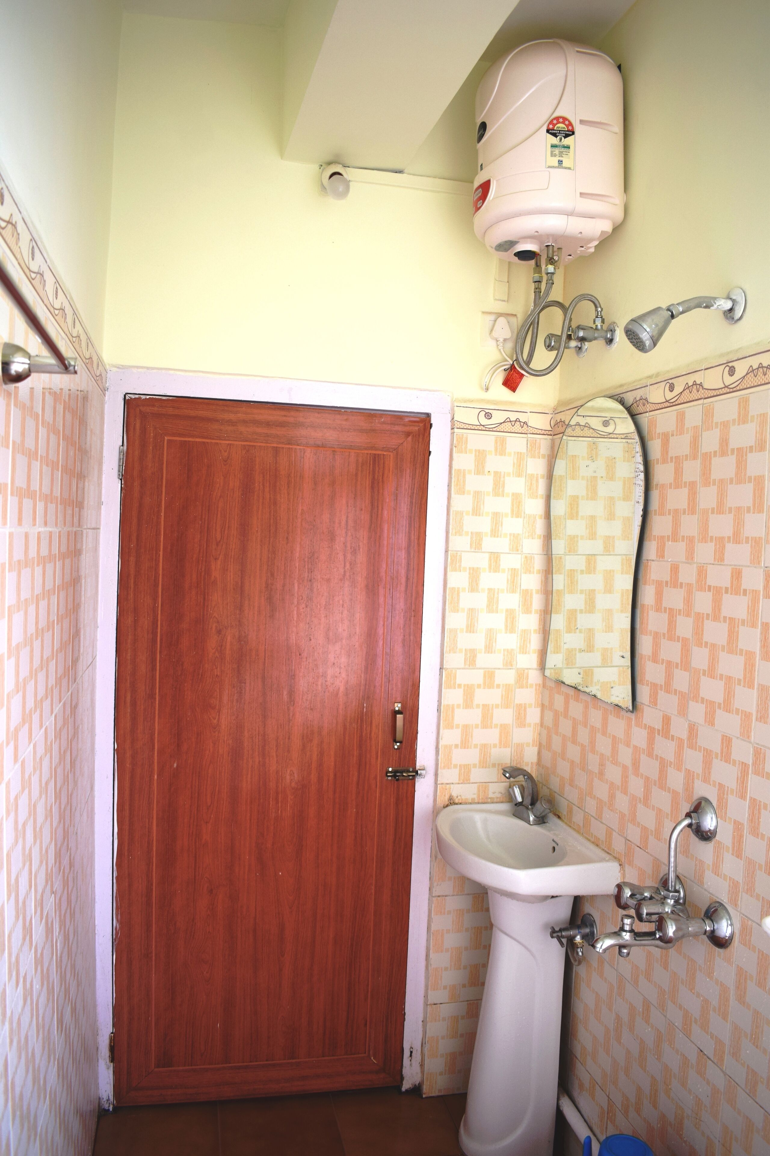 Un baño con puerta de madera, un lavabo blanco, un espejo y un calentador en la pared.
