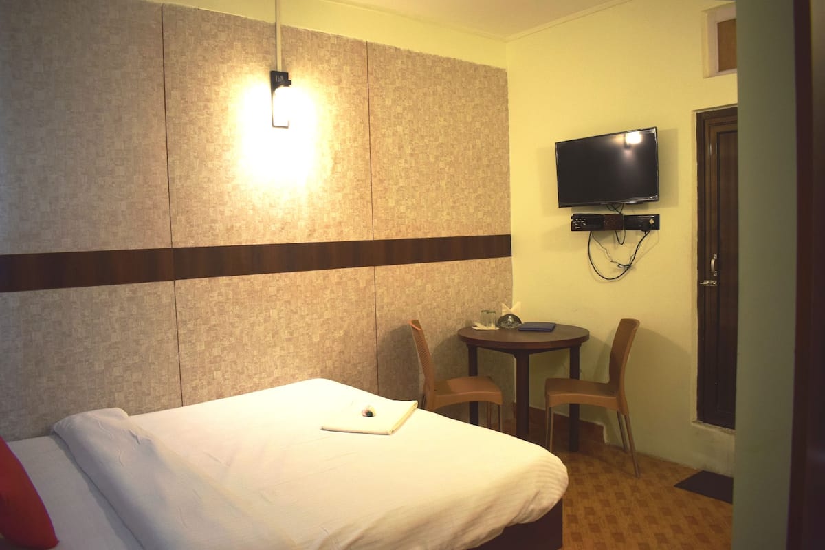 A hotel room with a bed, a desk, a chair, a TV, and a door.