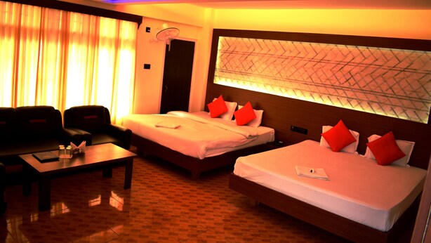 Una habitación de hotel con dos camas, un sofá, una mesa y un amplio ventanal con cortinas.