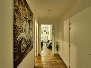 A hallway with a wooden floor, a door on the right, and a painting on the left.
