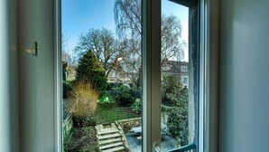Uitzicht vanaf een balkon met een stenen trap die leidt naar een tuin, omgeven door bomen en een heldere lucht.