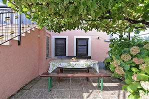 Un patio con una mesa y banco, rodeado de vegetación y un muro rosa.