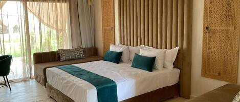 A spacious bedroom with a large bed, a ceiling fan, and a view of the outdoors through sheer curtains.