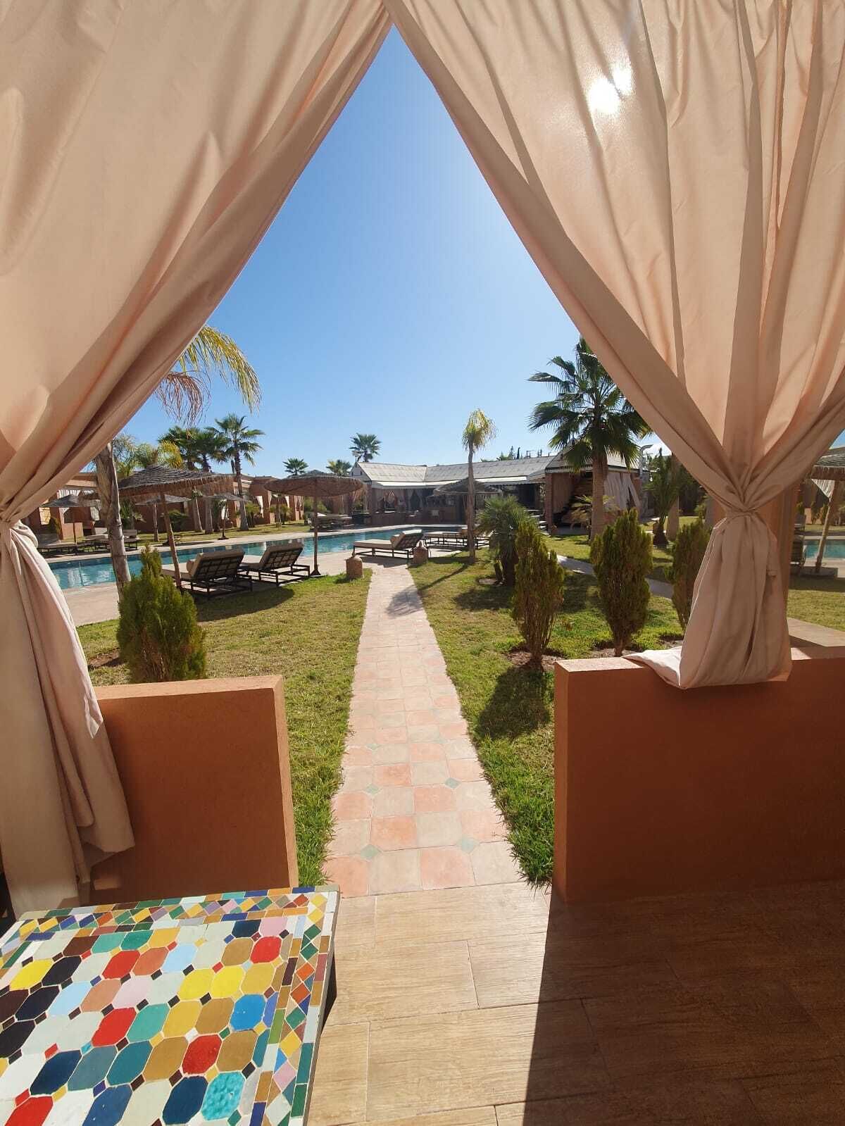 Vue prise depuis une zone aménagée avec des tentes, avec une piscine et des chaises longues en arrière-plan.