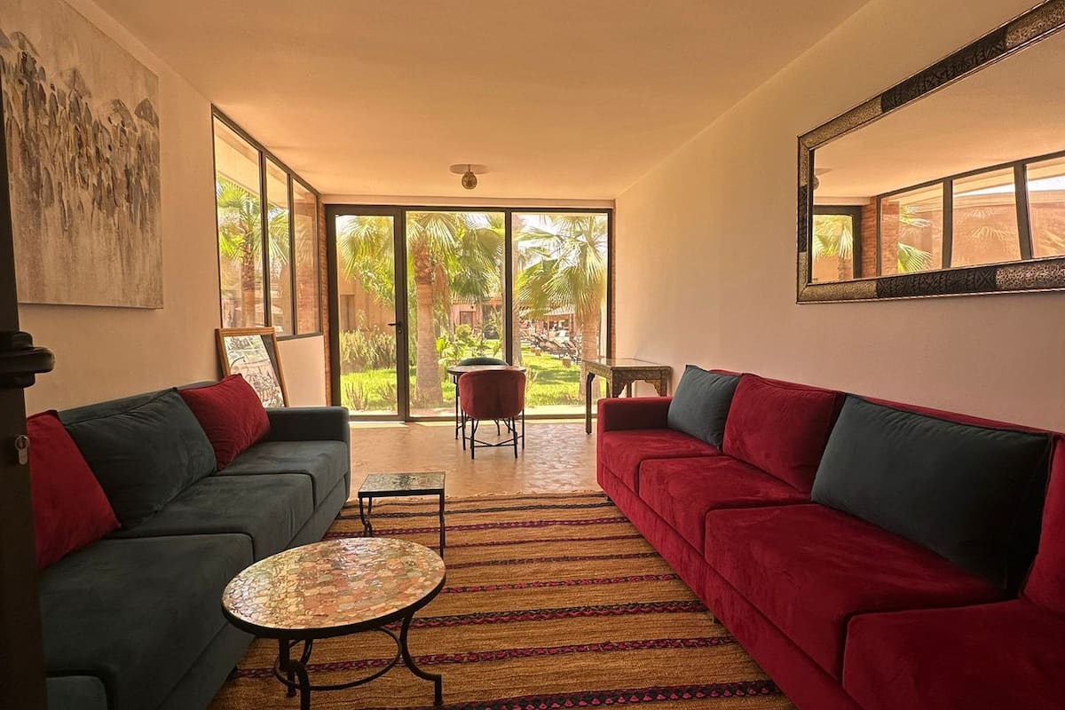 Ein geräumiges Wohnzimmer mit zwei Sofas, einem Couchtisch und Blick auf einen tropischen Garten durch große Fenster.
