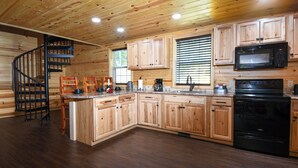 Una cocina con armarios de madera, un microondas negro, una estufa y una escalera espiral de madera.