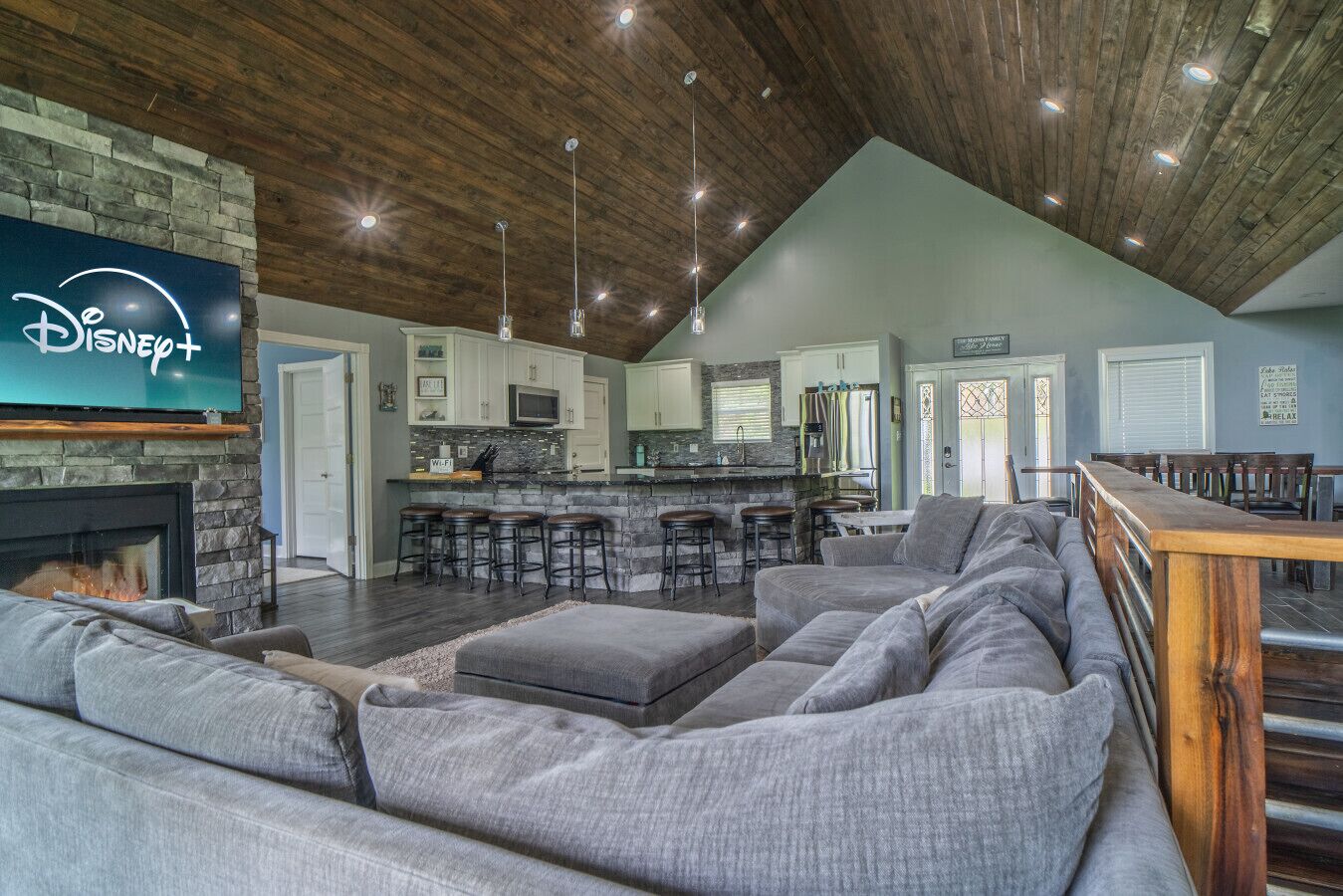 Uma sala de estar ampla com lareira, um sofá seccional cinza grande e um espaço bar com banquetas.